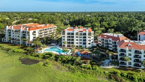 A resort with multiple buildings, a central swimming pool, and lush greenery.