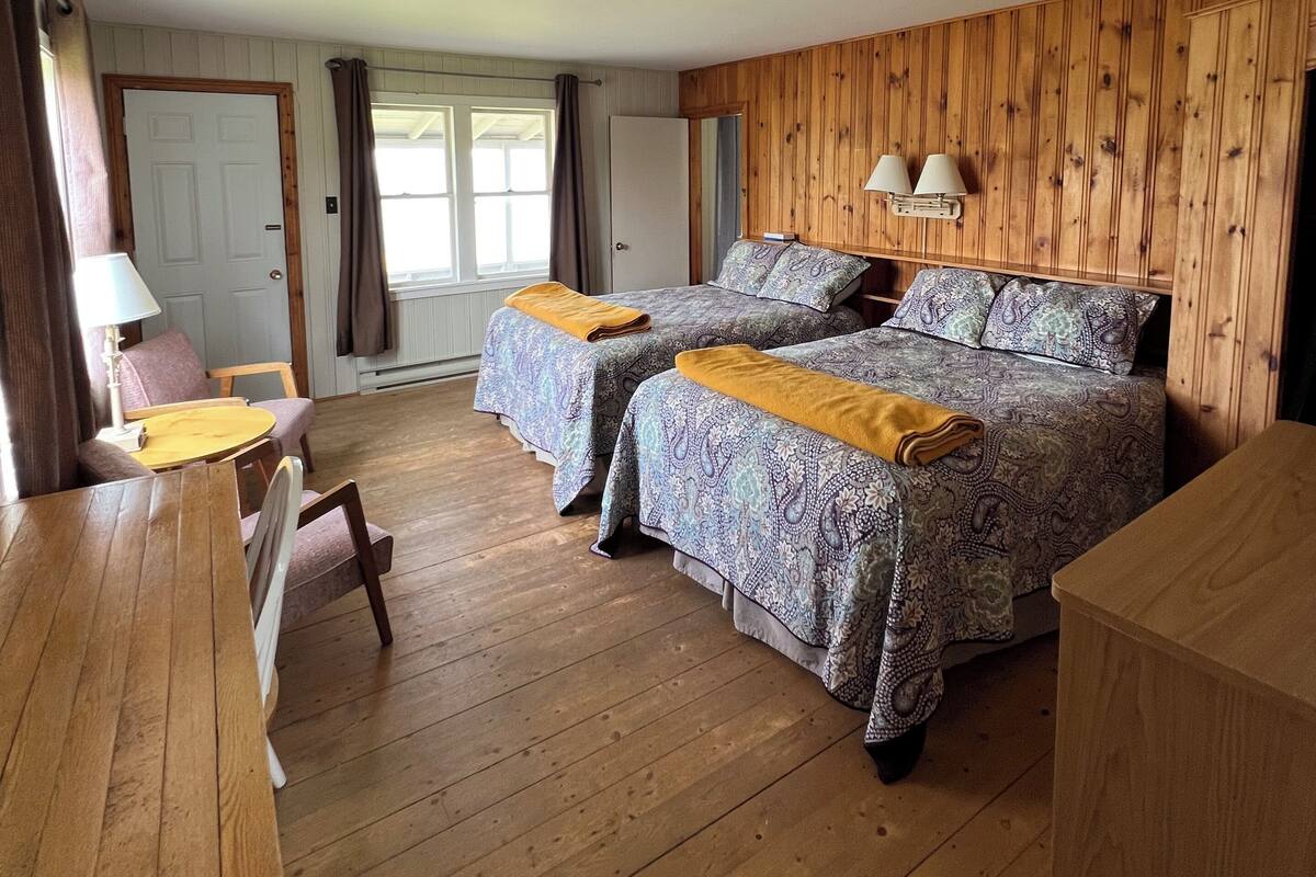 Una habitación con dos camas, una mesa de madera y una silla.