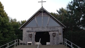 Una iglesia de madera con una cruz en la parte superior, un porche con decoraciones en forma de corazón y una escalera que conduce a la entrada.