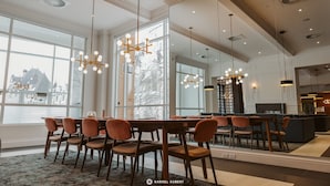 A spacious dining area with a long table and multiple chairs, large windows offering a view of a cityscape, and modern pendant lighting. - Hotel Chateau Laurier Quebec (Québec City)