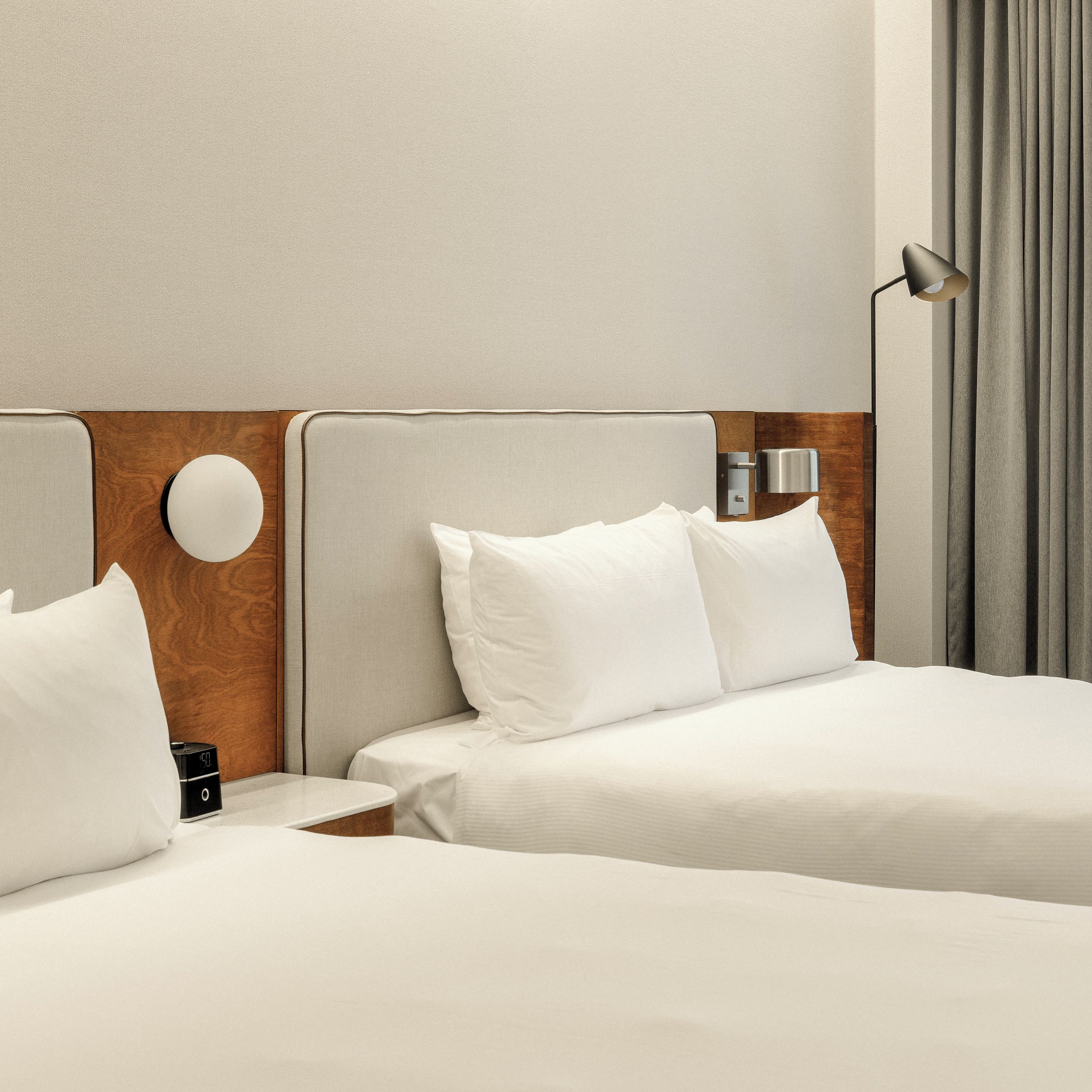Una habitación de hotel con dos camas, una mesita de noche con un reloj y una lámpara.