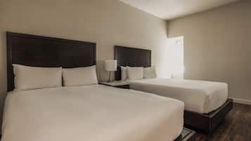 Une chambre d’hôtel avec deux lits, une table de chevet avec une lampe et une fenêtre laissant entrer la lumière naturelle.