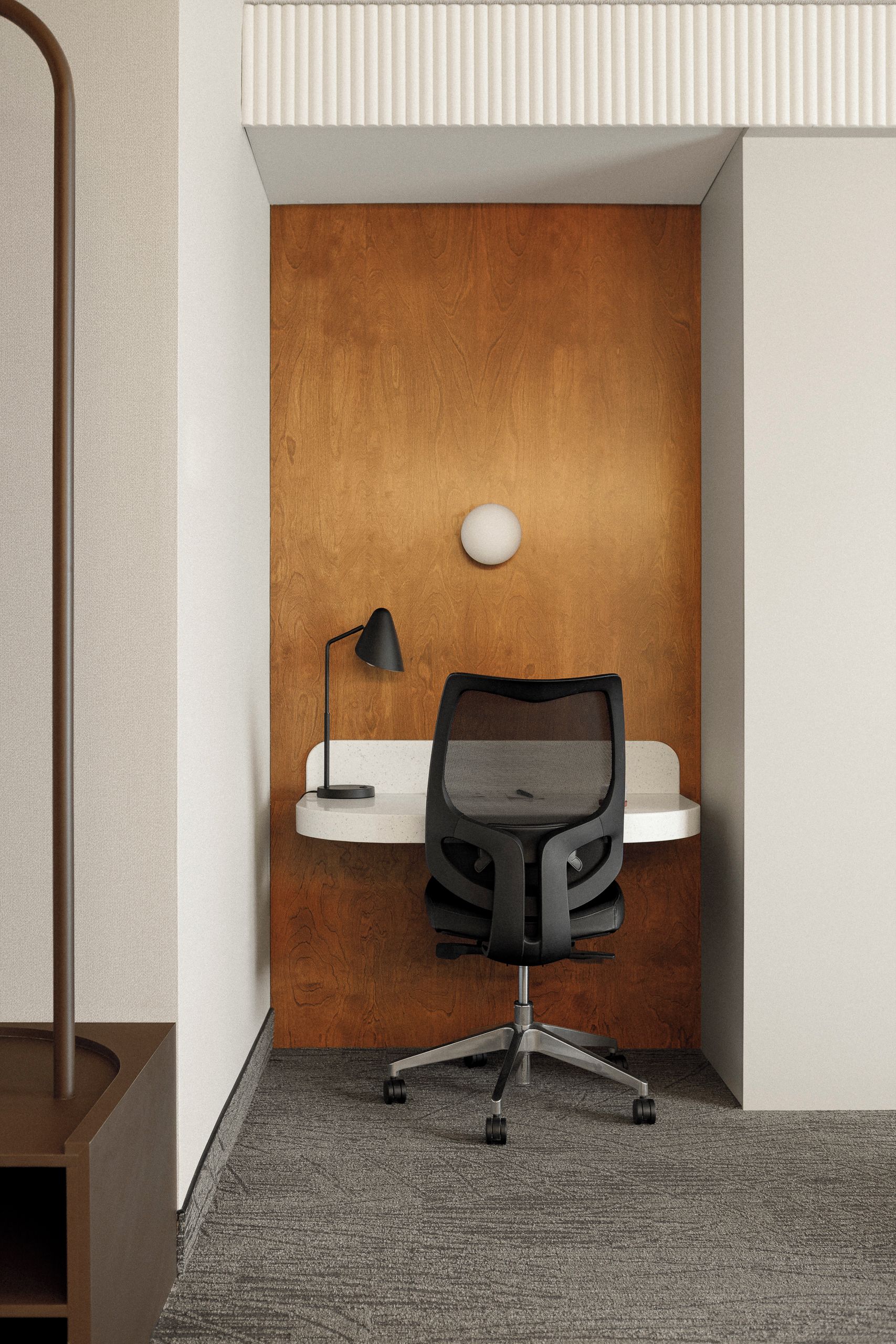 A corner office with a desk, chair, lamp, and a wall-mounted light fixture.