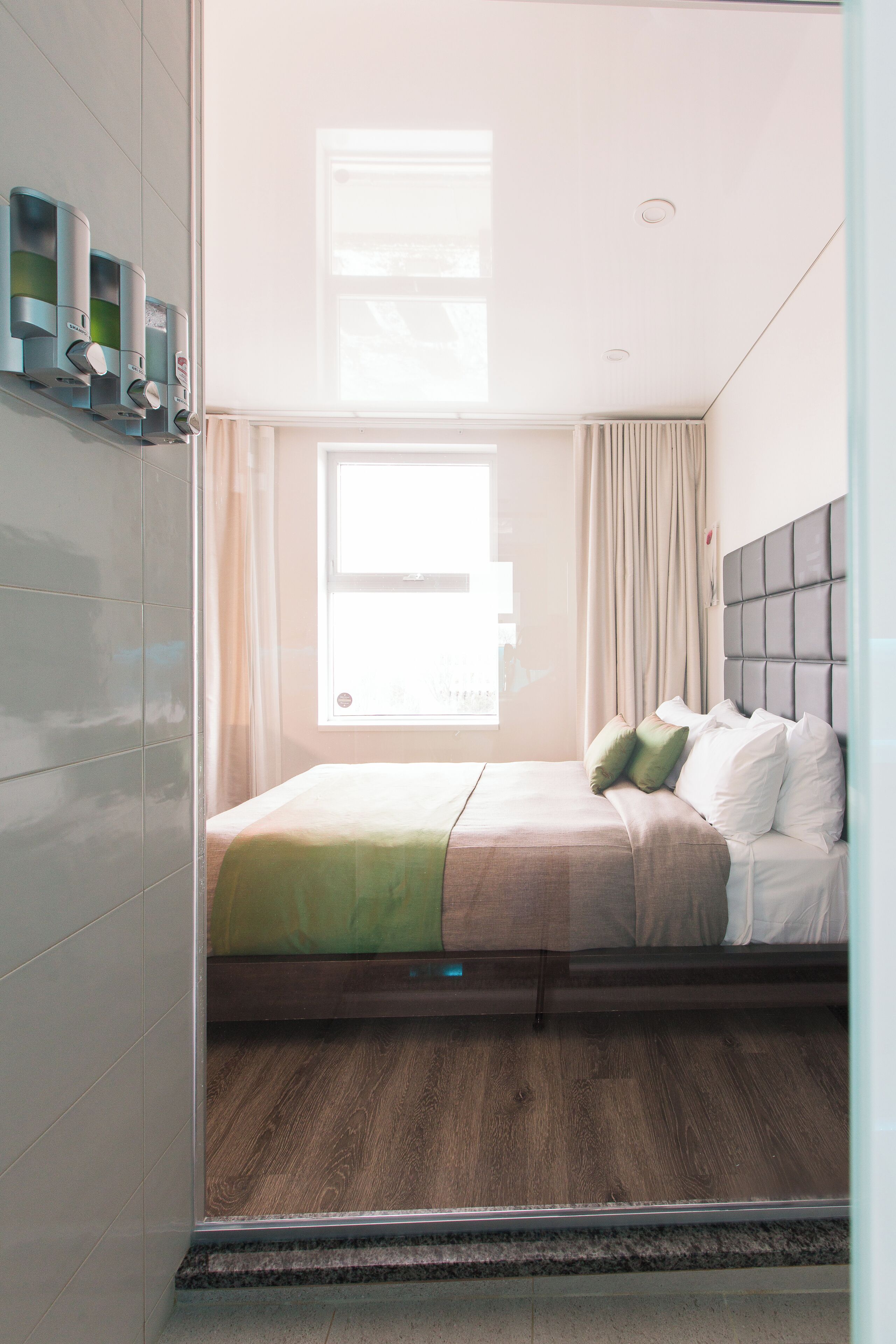 Ein Hotelzimmer mit Bett, Fenster, Vorhang und wandmontiertem Luftreiniger.