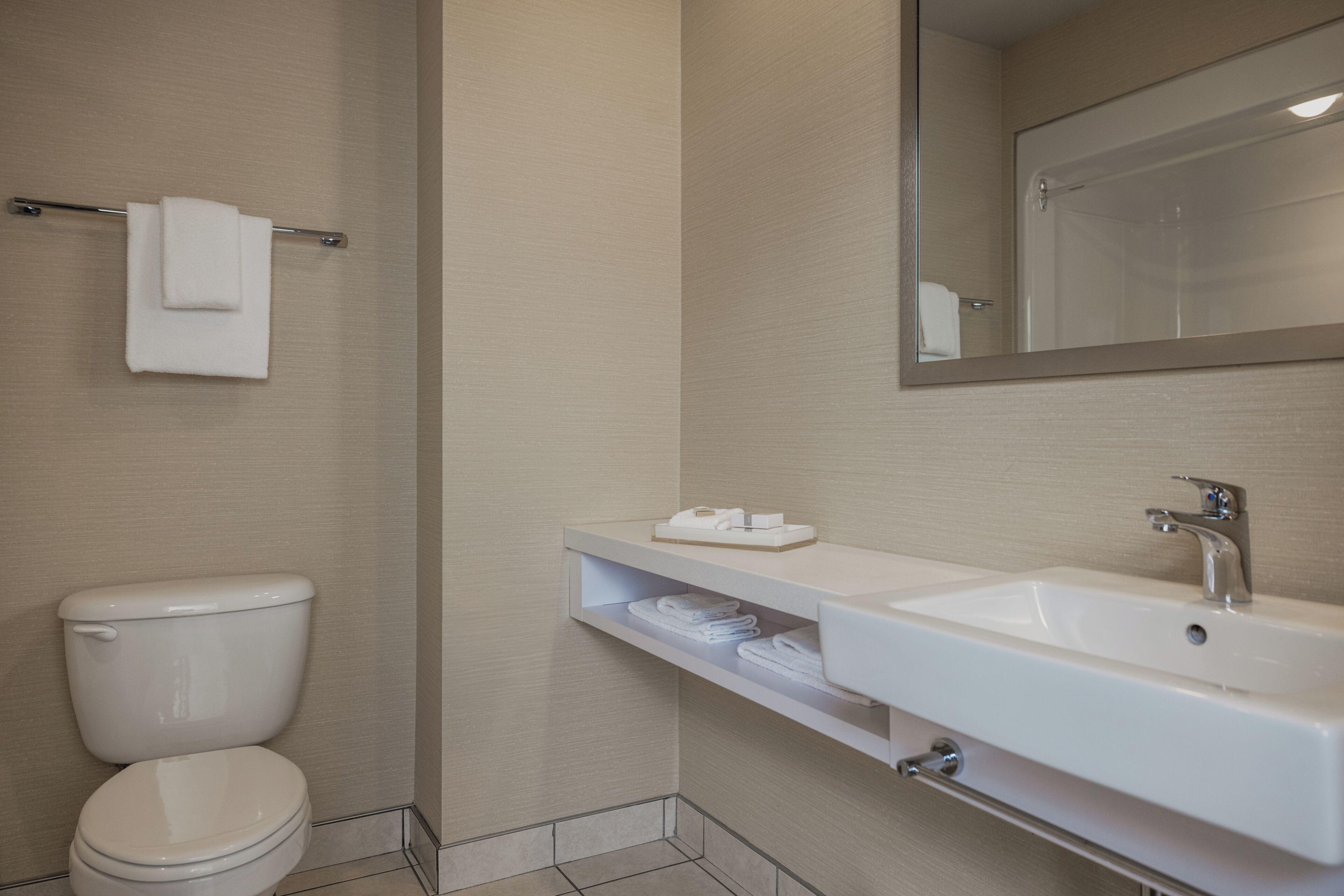 A bathroom with a toilet, sink, mirror, towel rack, and shelf with towels.