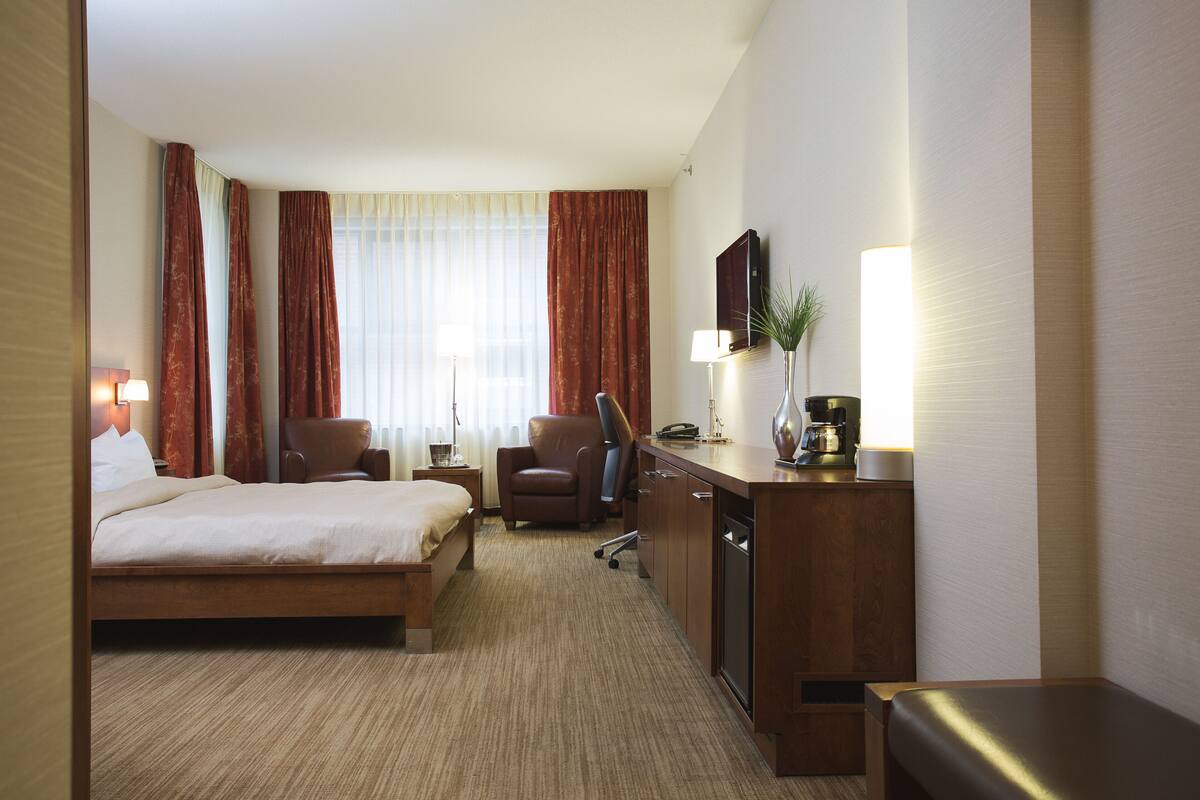 Ein Hotelzimmer mit Bett, Schreibtisch, Stuhl, Lampe und Fernseher.