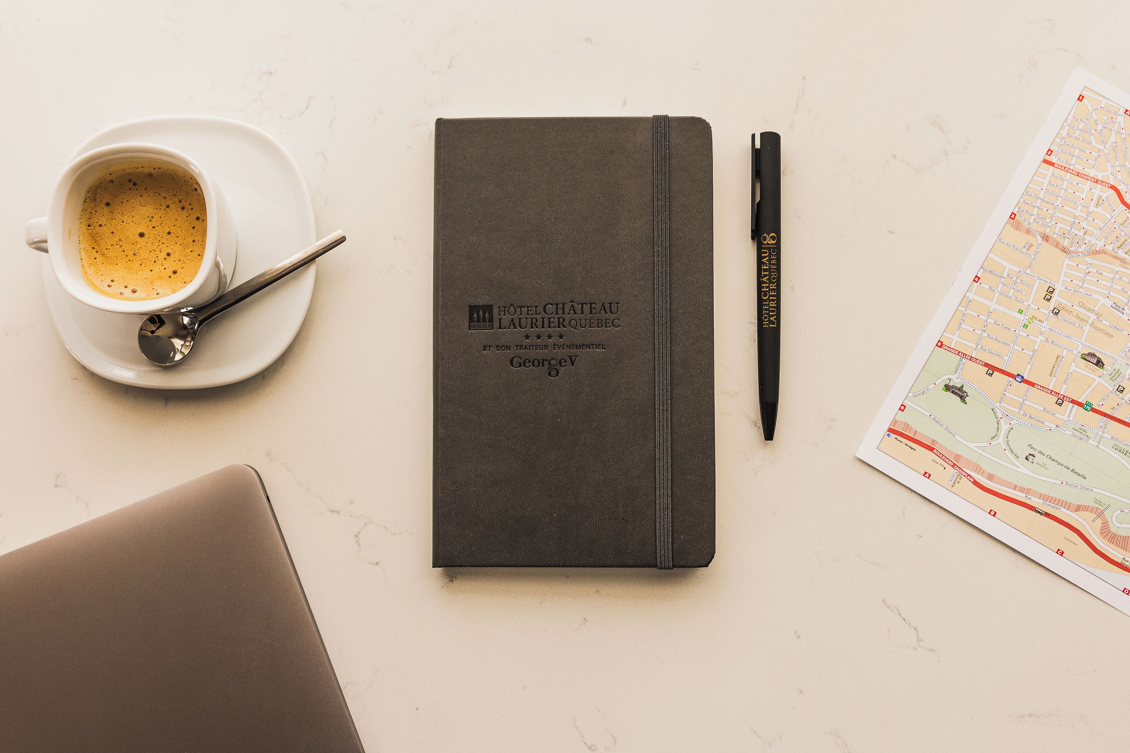 Un cuaderno con el logotipo de un hotel, un bolígrafo, una taza de café y un mapa.
