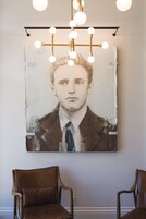 Une pièce ornée d’un grand portrait au mur, de deux chaises en bois et d’un lustre moderne.