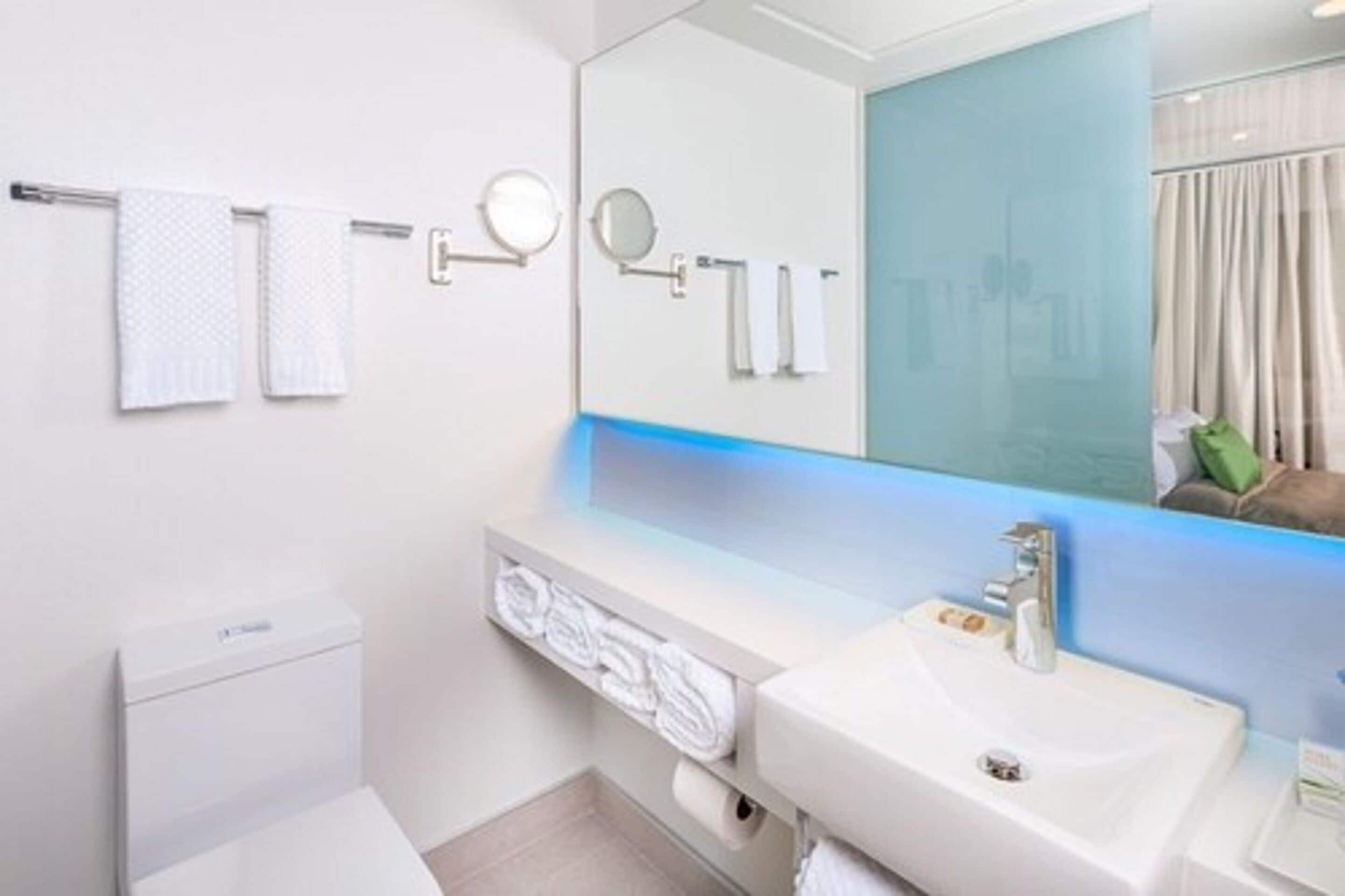 Un baño moderno con un lavabo blanco, un espejo grande y dos toallas colgadas en un perchero.