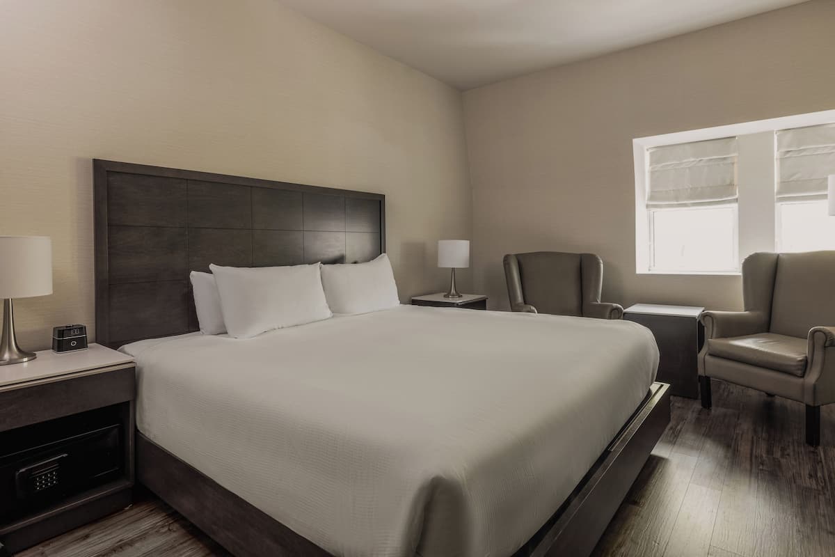 Ein Hotelzimmer mit einem großen Bett, zwei Nachttischen, einem Sessel und einem Fenster mit Jalousien.