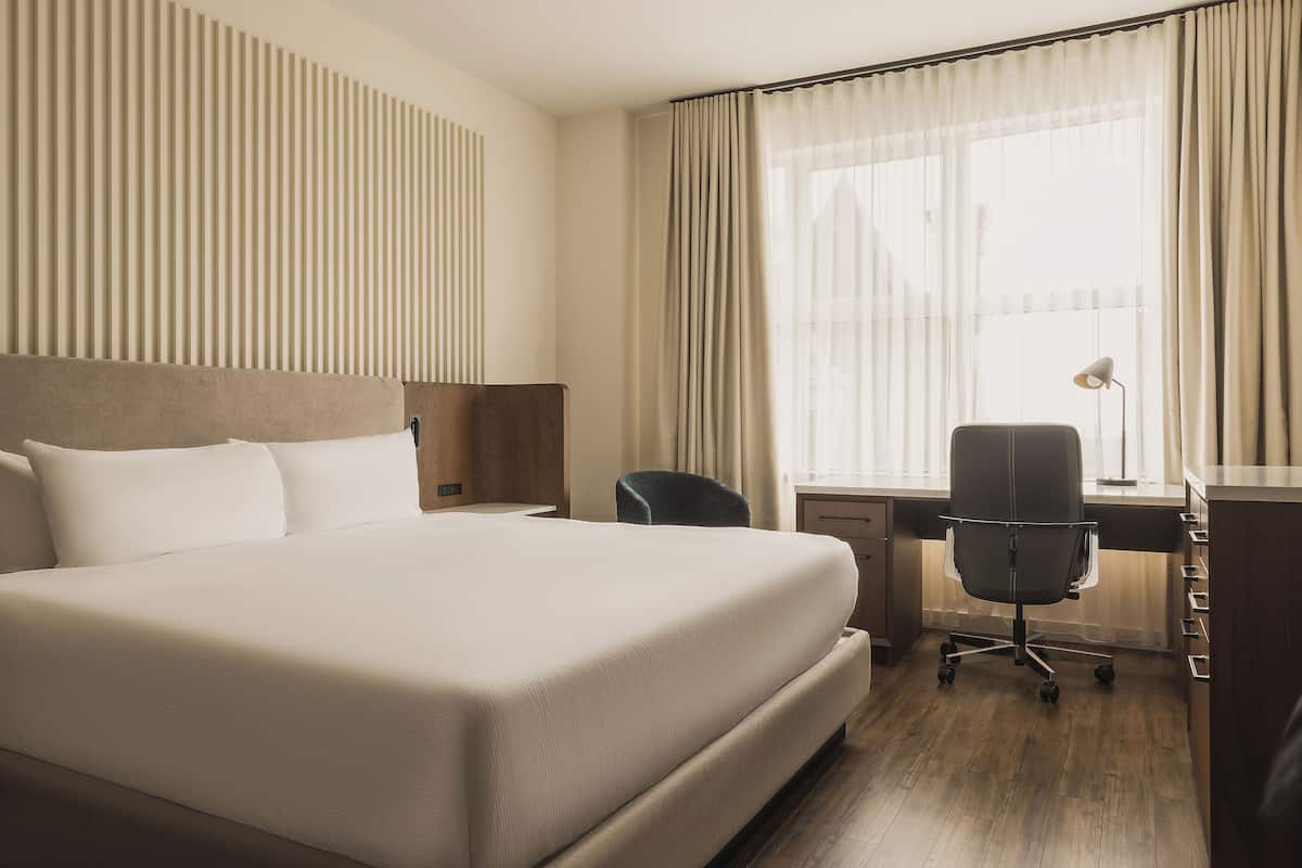 Ein Hotelzimmer mit einem großen Bett, einem Schreibtisch, einem Sessel und einer Lampe.