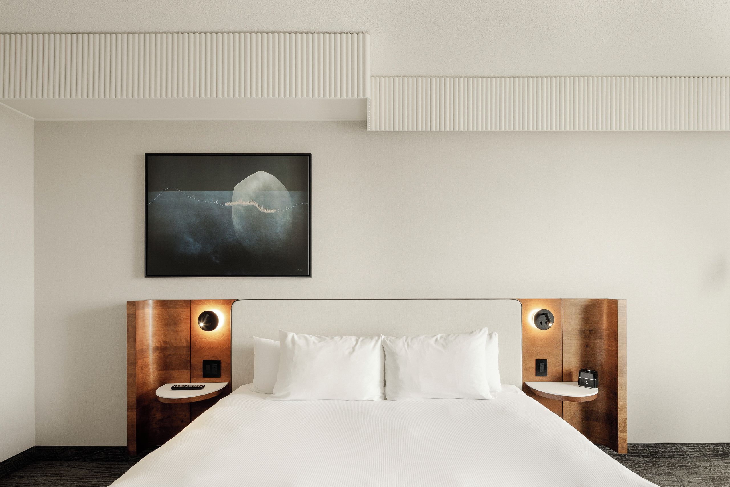 A hotel room with a bed, two bedside tables, a wall-mounted artwork, and a ceiling with a textured design.