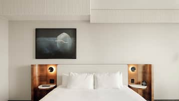 A hotel room with a bed, two bedside tables, a wall-mounted artwork, and a ceiling with a textured design.