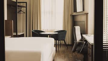 A hotel room with a bed, a desk, two chairs, a TV, and a window with curtains.