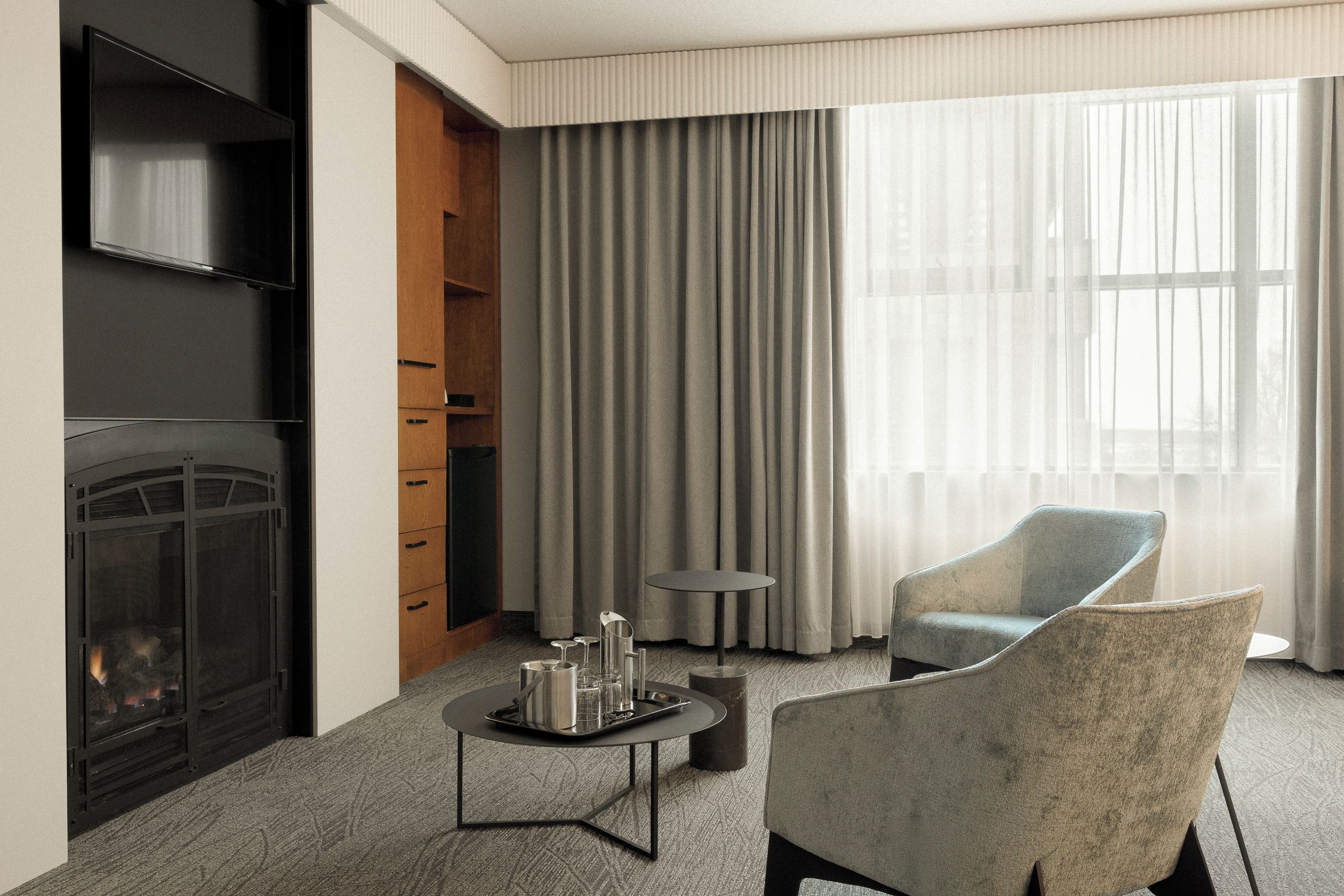 A hotel room with a fireplace, a seating area with a table, and a large window with curtains.