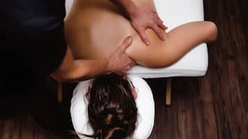 A person receiving a back massage on a white massage table in a room with wooden flooring.