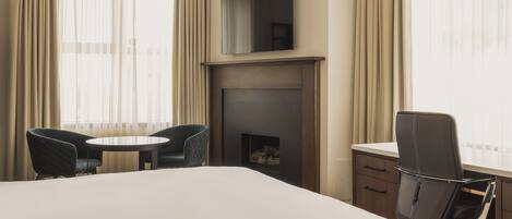 A hotel room with a large bed, a desk with a chair, a fireplace, and a TV mounted on the wall.