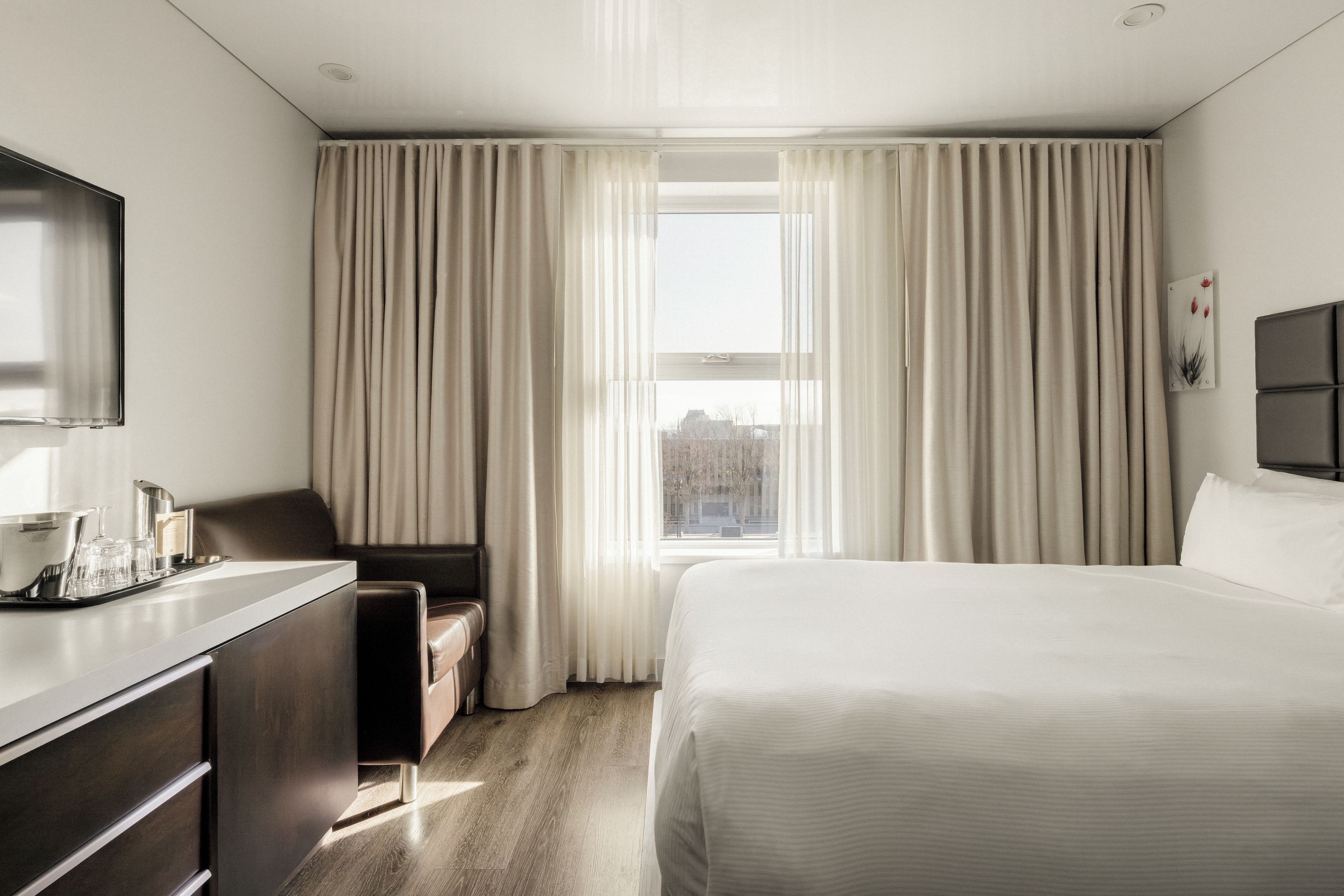 Una habitación de hotel con cama, escritorio, silla y ventana con cortinas.