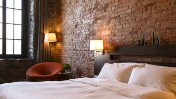 A hotel room with a brick wall, a bed with white linens, a red chair, and two wall-mounted lamps.