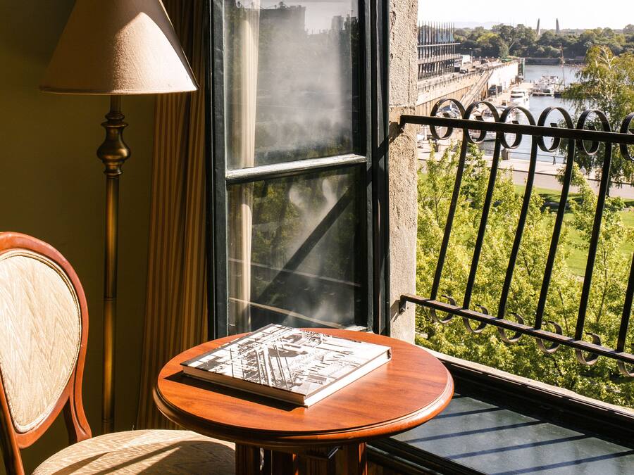 A balcony with a view of a bridge and river, a table with a book, a chair, and a lamp.