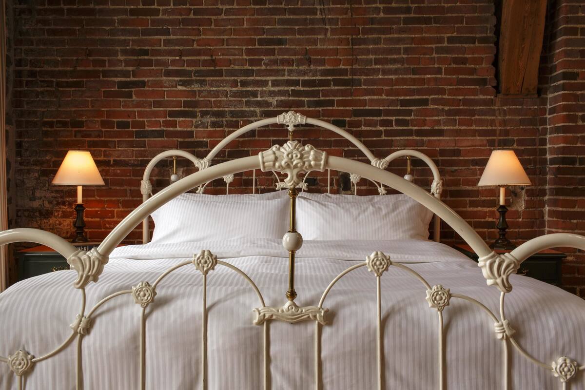 A bed with a white metal frame and a brick wall background.