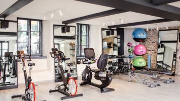 A gym with exercise equipment, mirrors, and a stone wall.