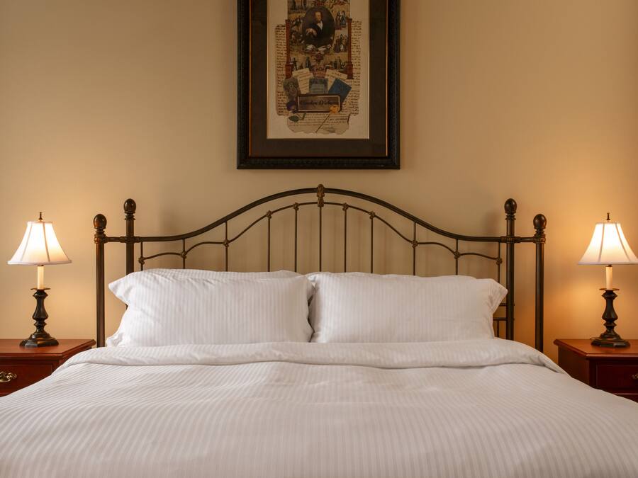 A neatly made bed with white linens, two bedside tables with lamps, and a framed picture on the wall.