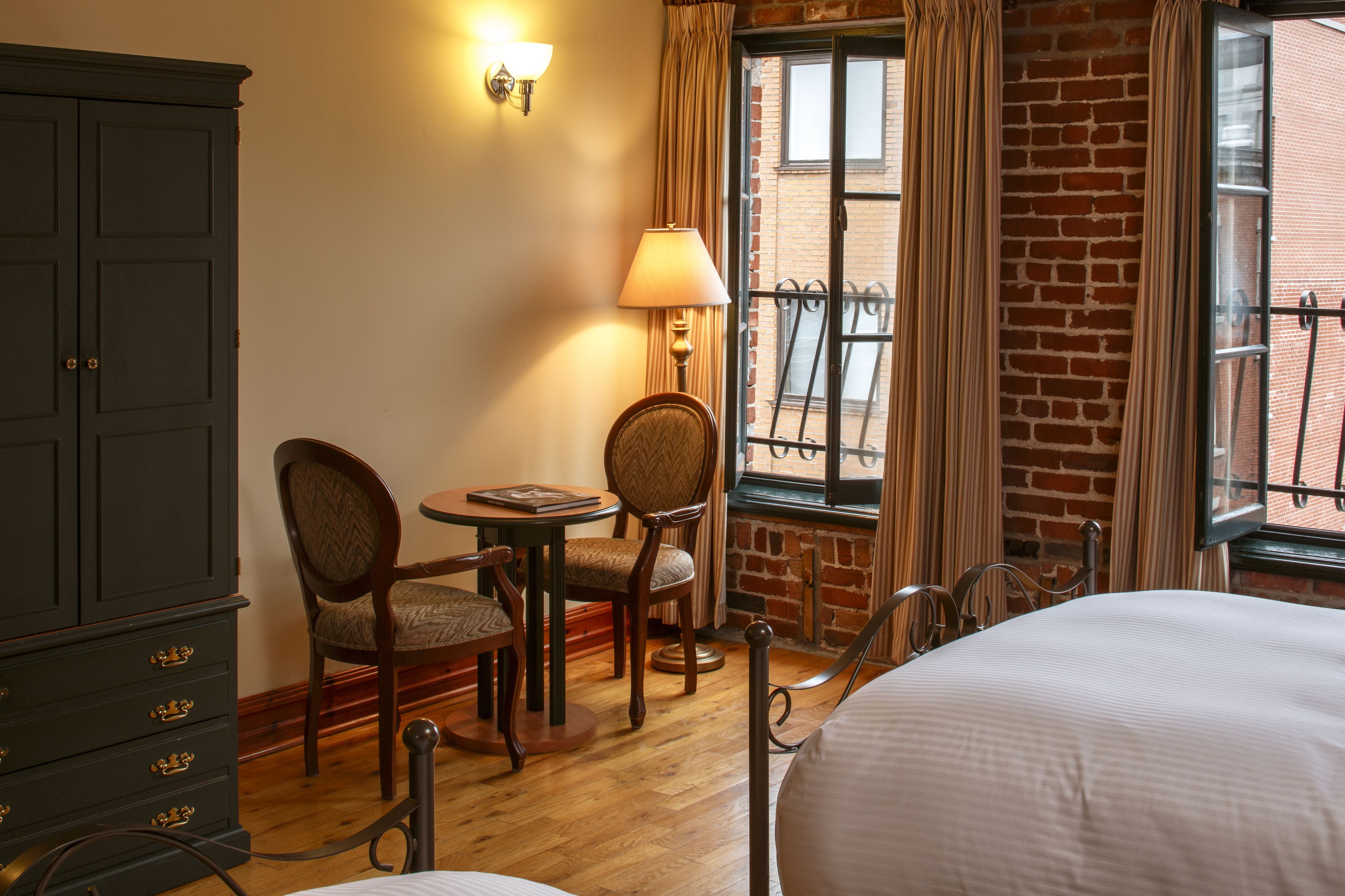 Una camera d'albergo con un letto, una scrivania con sedie, una lampada e un armadio.