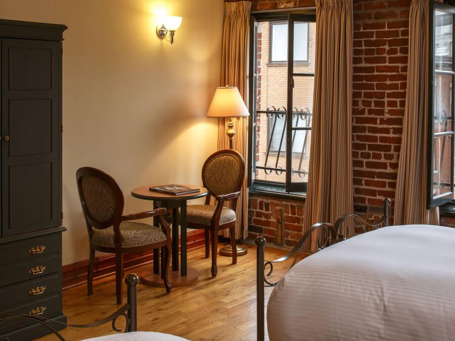 Una camera d'albergo con un letto, una scrivania con sedie, una lampada e un armadio.