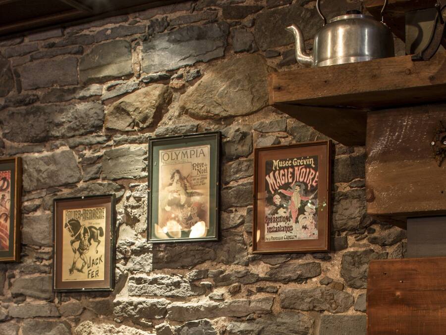 Pared de piedra con carteles enmarcados y una tetera sobre una estantería.