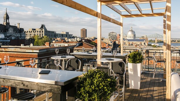 An outdoor terrace with tables and chairs, overlooking a cityscape with historic buildings and a bridge. - Auberge du Vieux-Port (Montreal)
