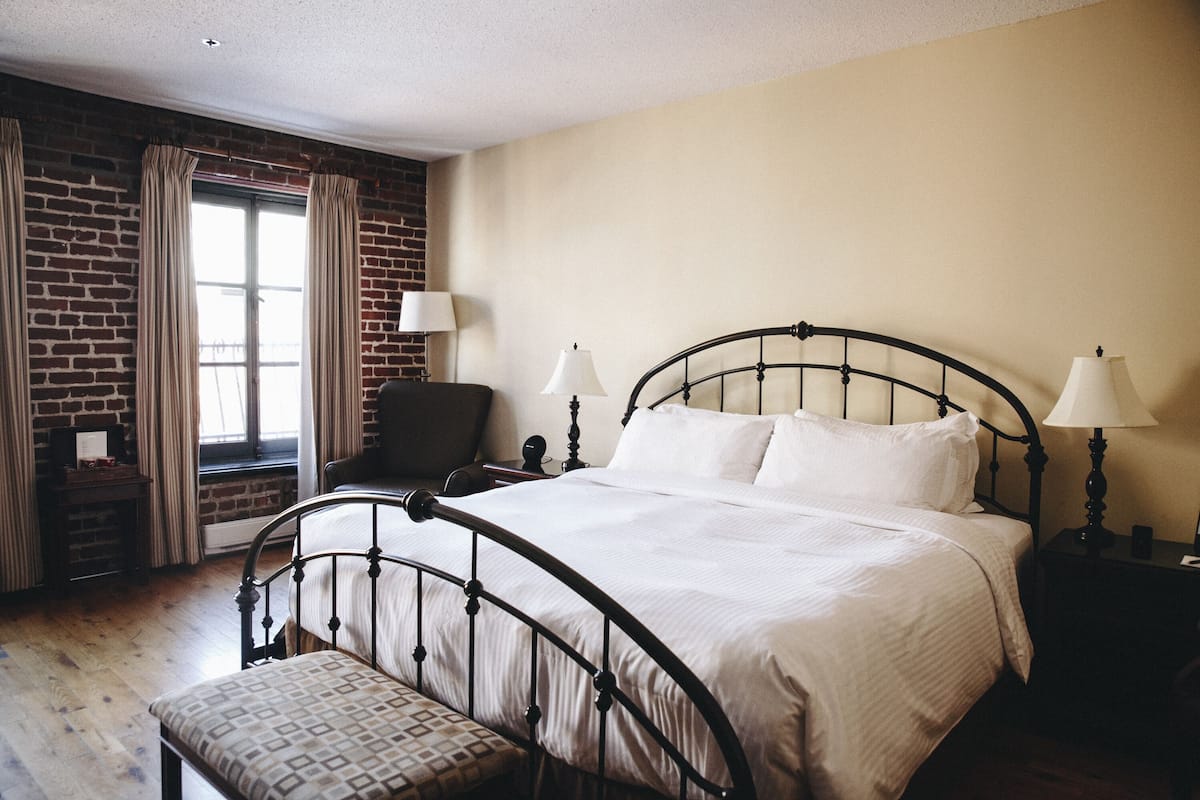 A neatly arranged bedroom with a bed, bedside lamps, a chair, and a window with curtains.