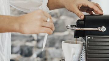 A person operating a coffee machine, with a cup and a plate with a coffee pod and spoon on a wooden table.