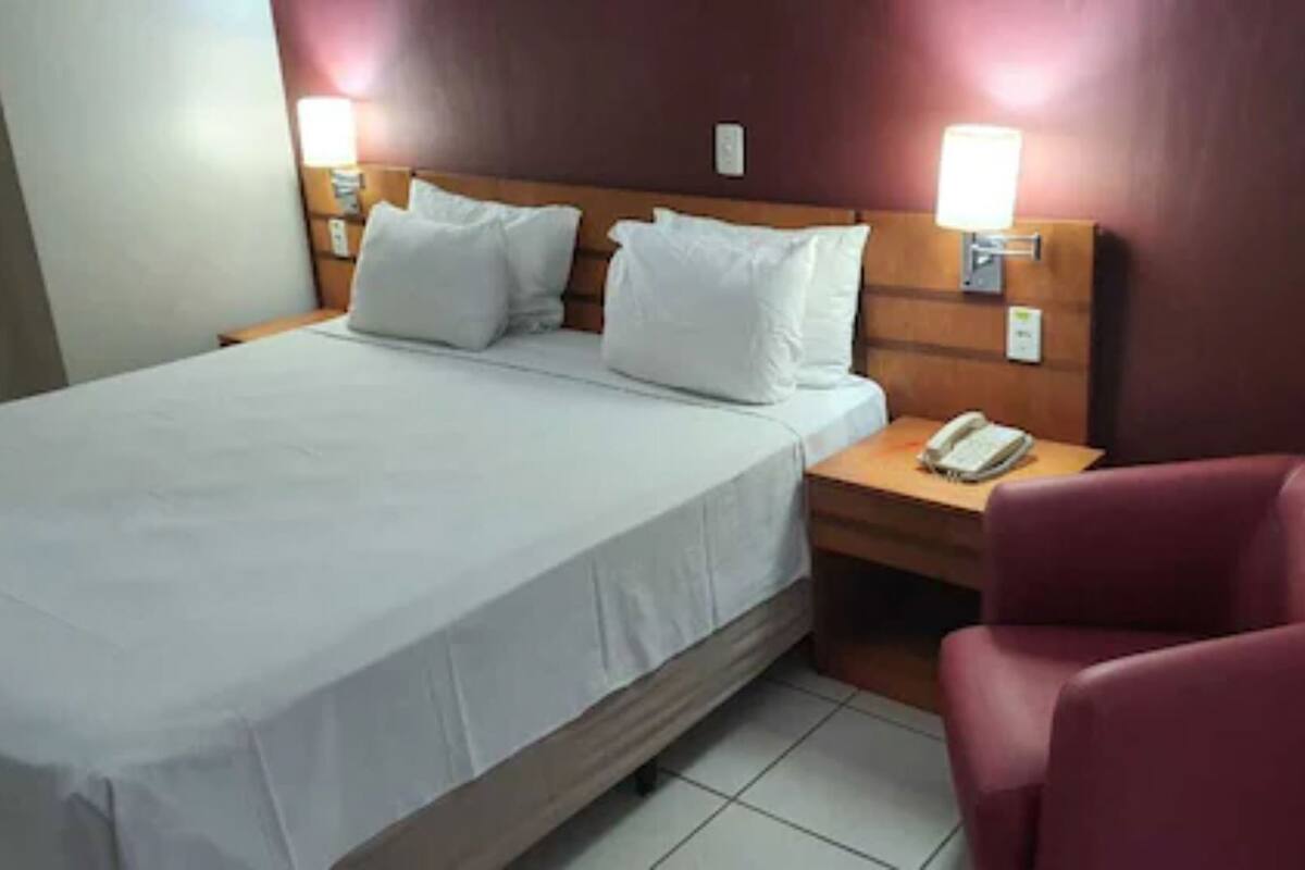 Une chambre d’hôtel avec un lit, une table de chevet avec un téléphone et une chaise rouge.