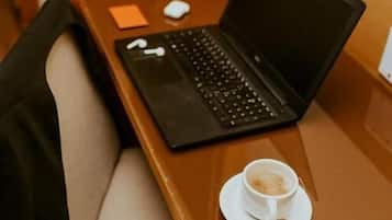Um laptop sobre uma mesa de madeira, com uma chávena de café e um rato.