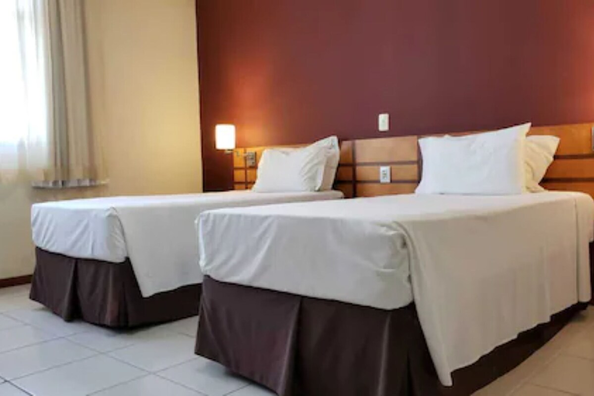 A hotel room with two beds, a wooden headboard, and a nightstand with a lamp.