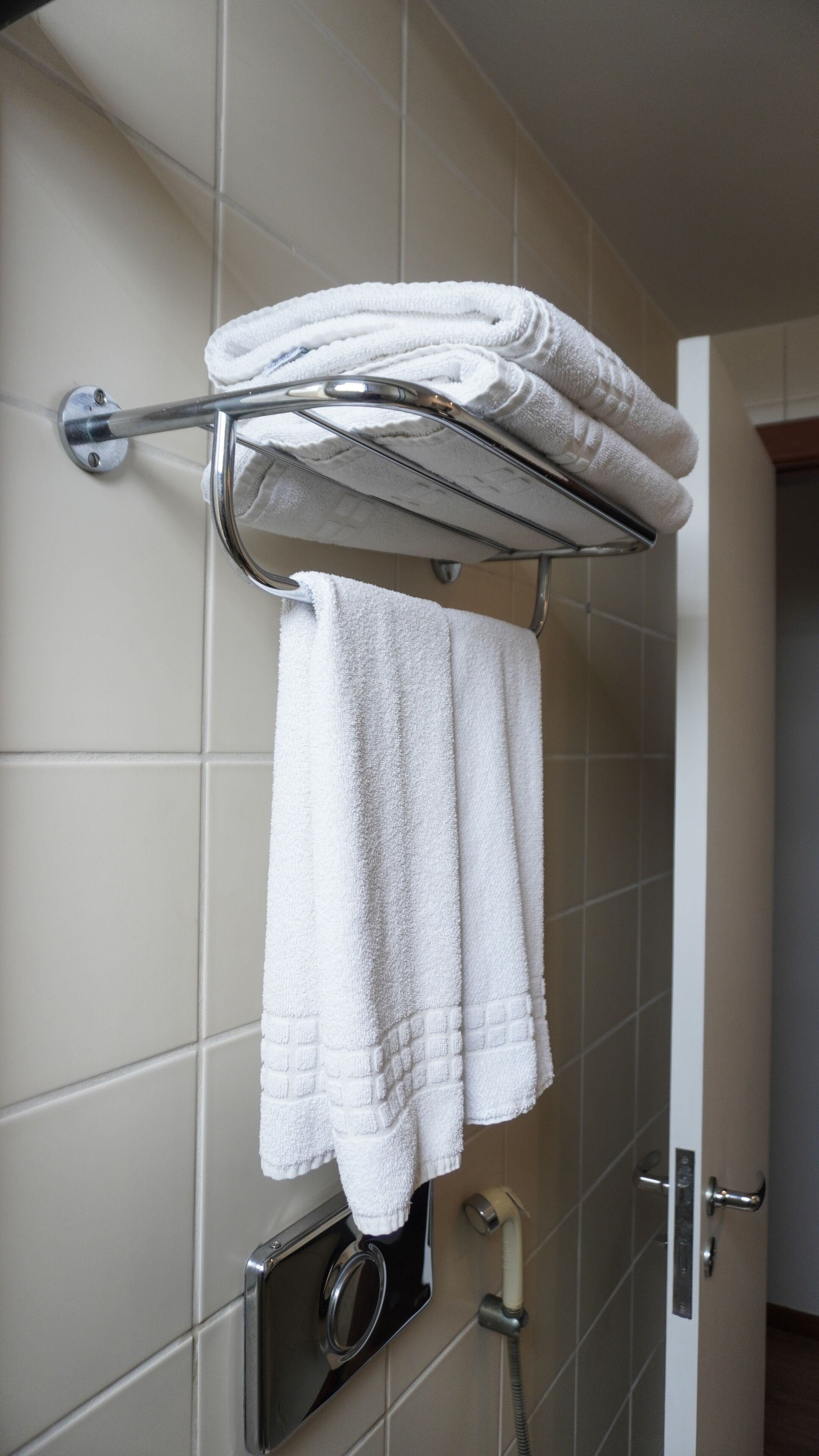 A bathroom with a towel rack holding folded towels, a shower control panel, and a door leading to another room.