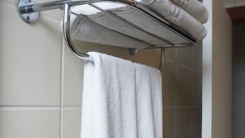A bathroom with a towel rack holding folded towels, a shower control panel, and a door leading to another room.