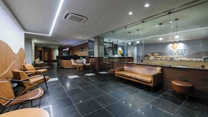 A modern hotel lobby with a reception desk, leather seating, and a kitchen area. - Vitória Praia (Vitoria)
