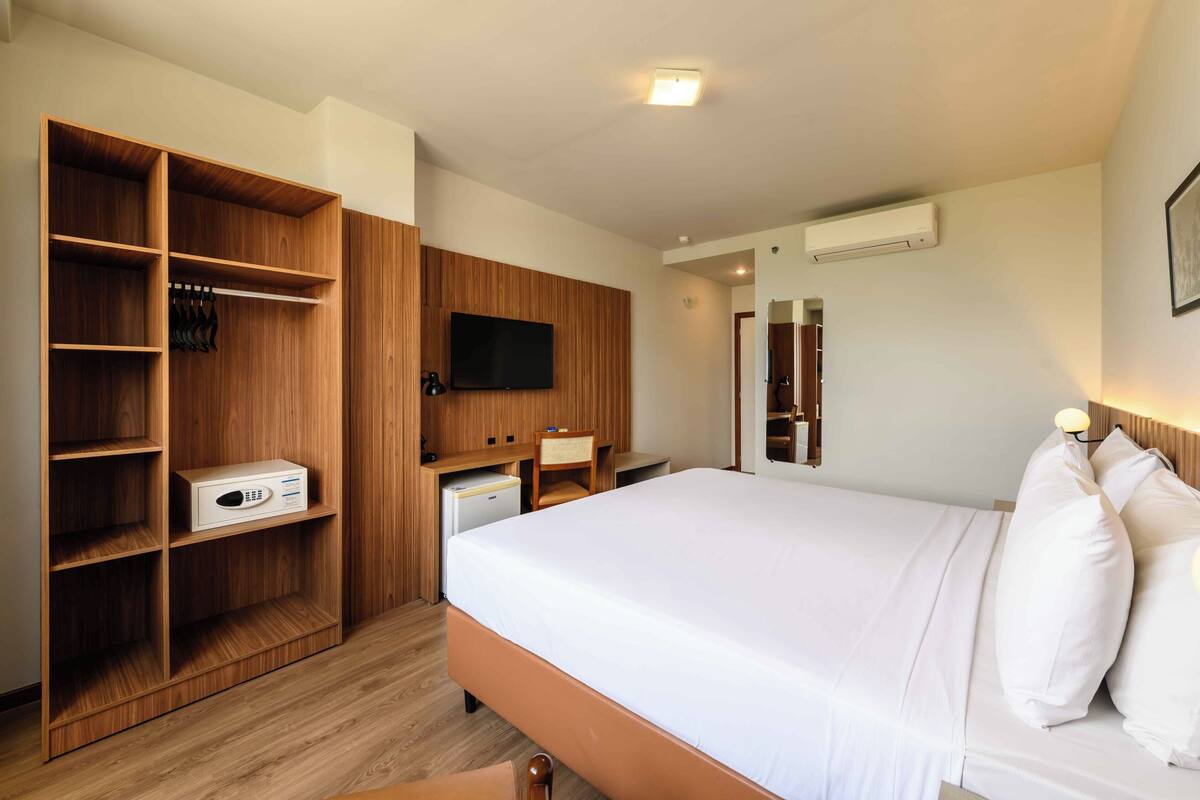 Une chambre d’hôtel avec un grand lit, une armoire en bois, un bureau et un téléviseur à écran plat.