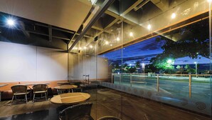 An outdoor seating area with tables and chairs, a glass partition, and a view of the street at night. - Vitória Praia (Vitoria)