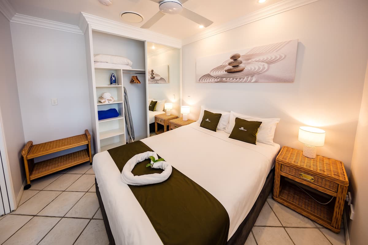 Habitación de hotel con cama, mesita de noche, espejo, armario y una obra de arte colgada en la pared.