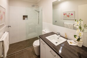 Ein modernes Badezimmer mit einer gläsernen Dusche, einem weißen Waschbecken und einer Topforchidee.