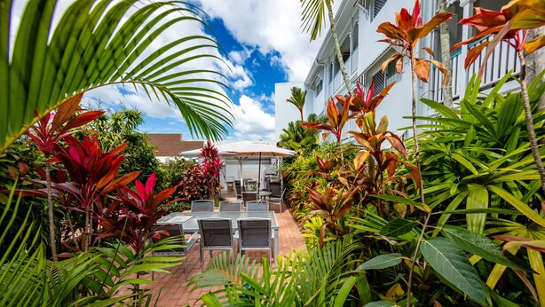 A patio area with tables and chairs, surrounded by lush tropical plants.