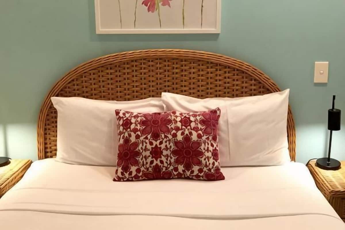 A bed with a woven headboard, white bedding, and a decorative pillow.