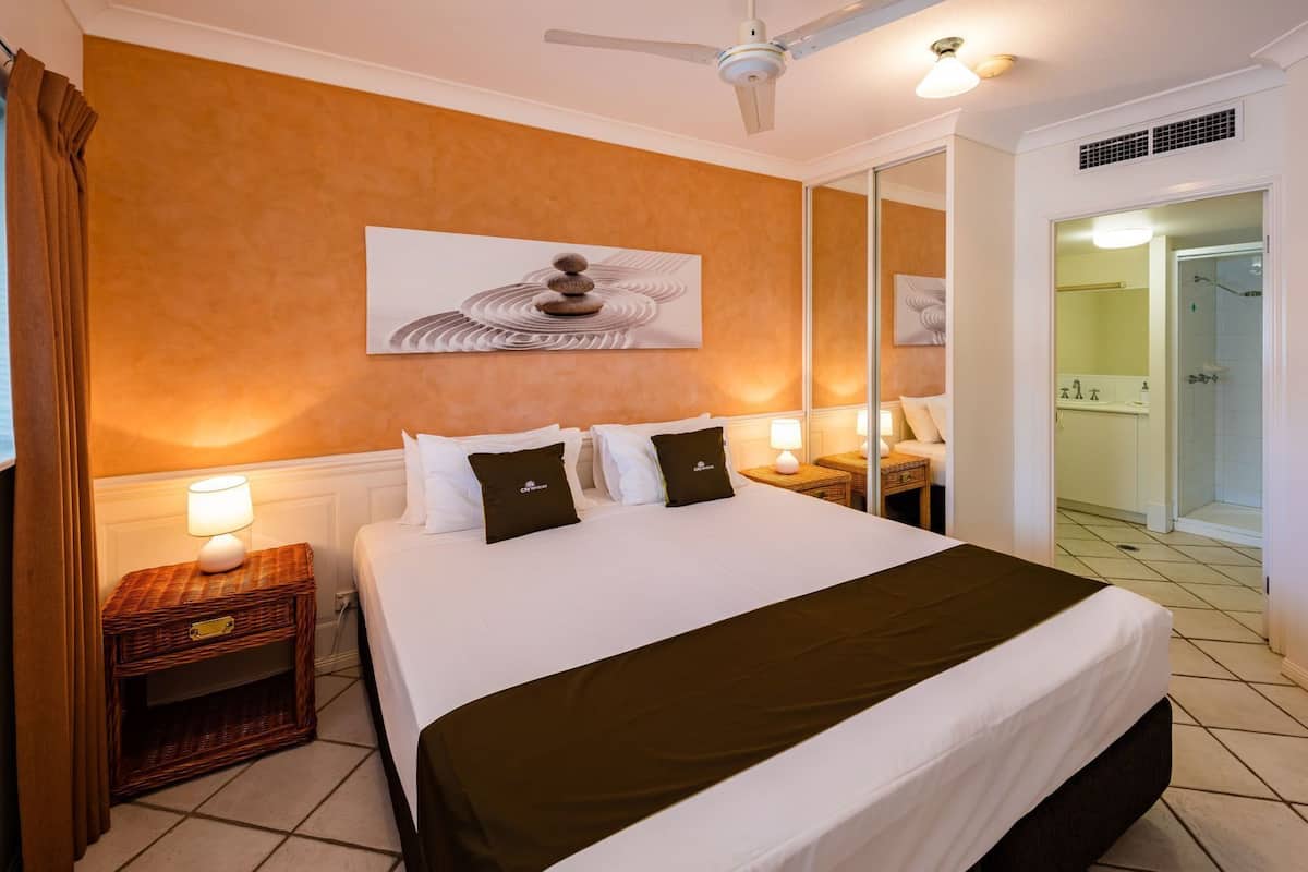 Una habitación de hotel con una cama, lámparas de noche, un espejo y vista al baño.