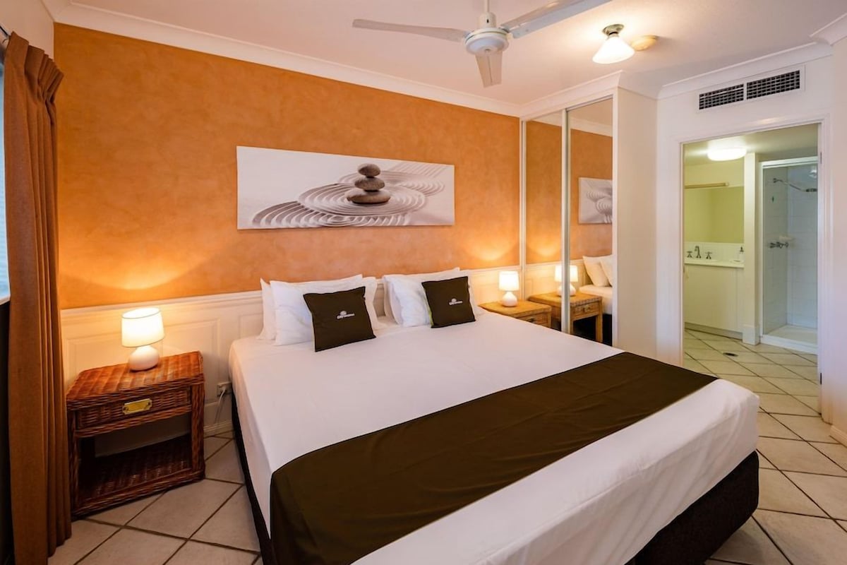 A hotel room with a bed, a nightstand, a mirror, and a door leading to a bathroom.