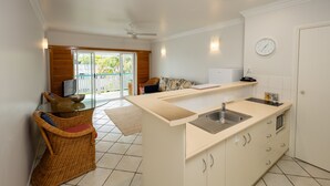 A modern kitchen with a central island, a dining area with a wicker chair, and a view of the outdoors.