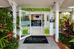 Der Eingang der City Terraces Holiday Apartments mit Empfangsbereich, Glastüren und grünen Sitzgelegenheiten.