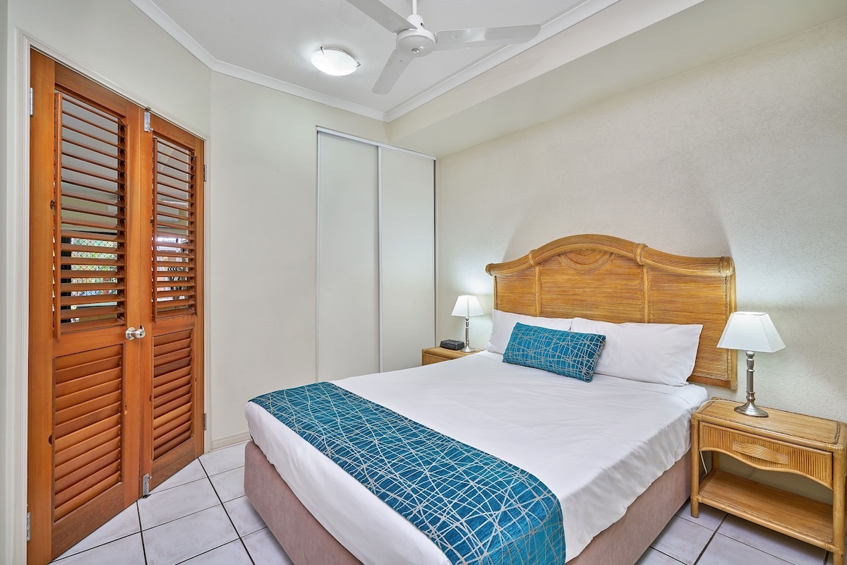A bedroom with a bed, wooden headboard, bedside lamps, and a ceiling fan.